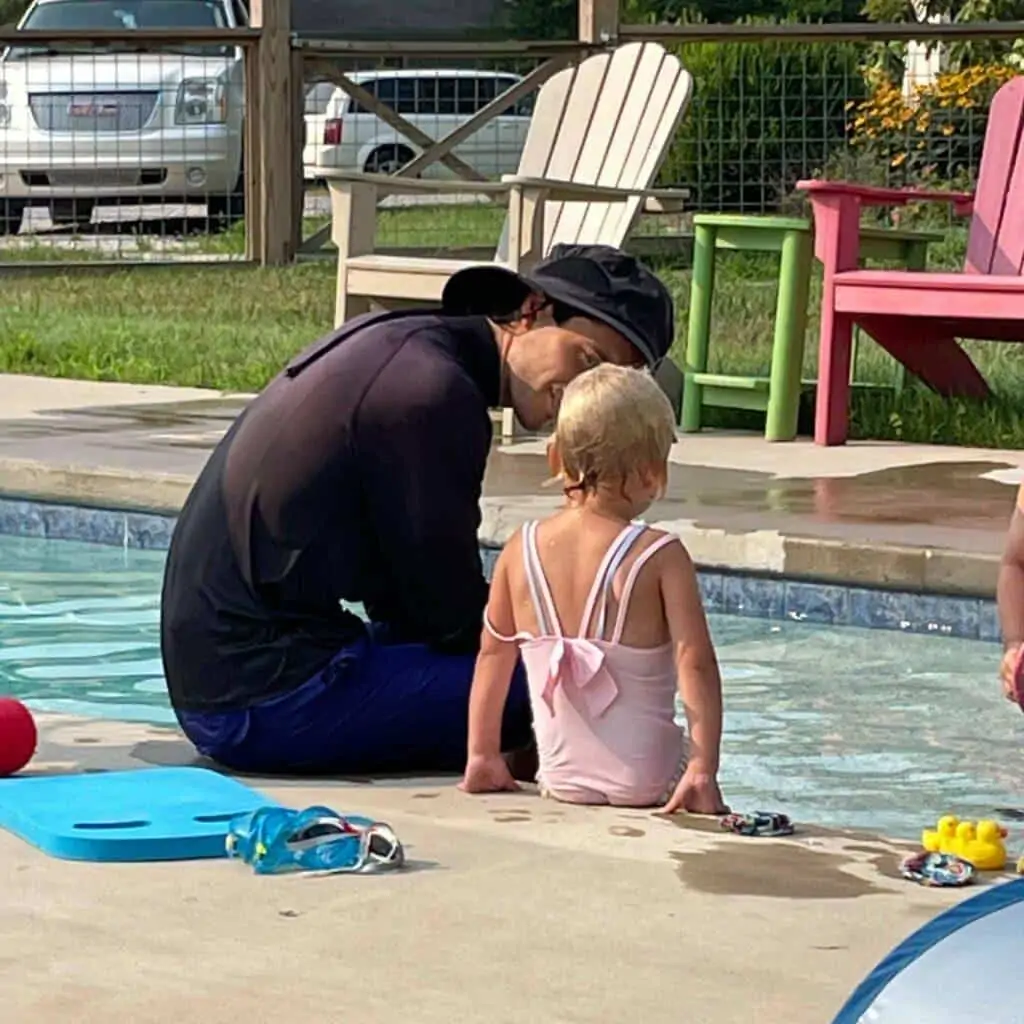 girl sitting by pool during swim lesson with adult